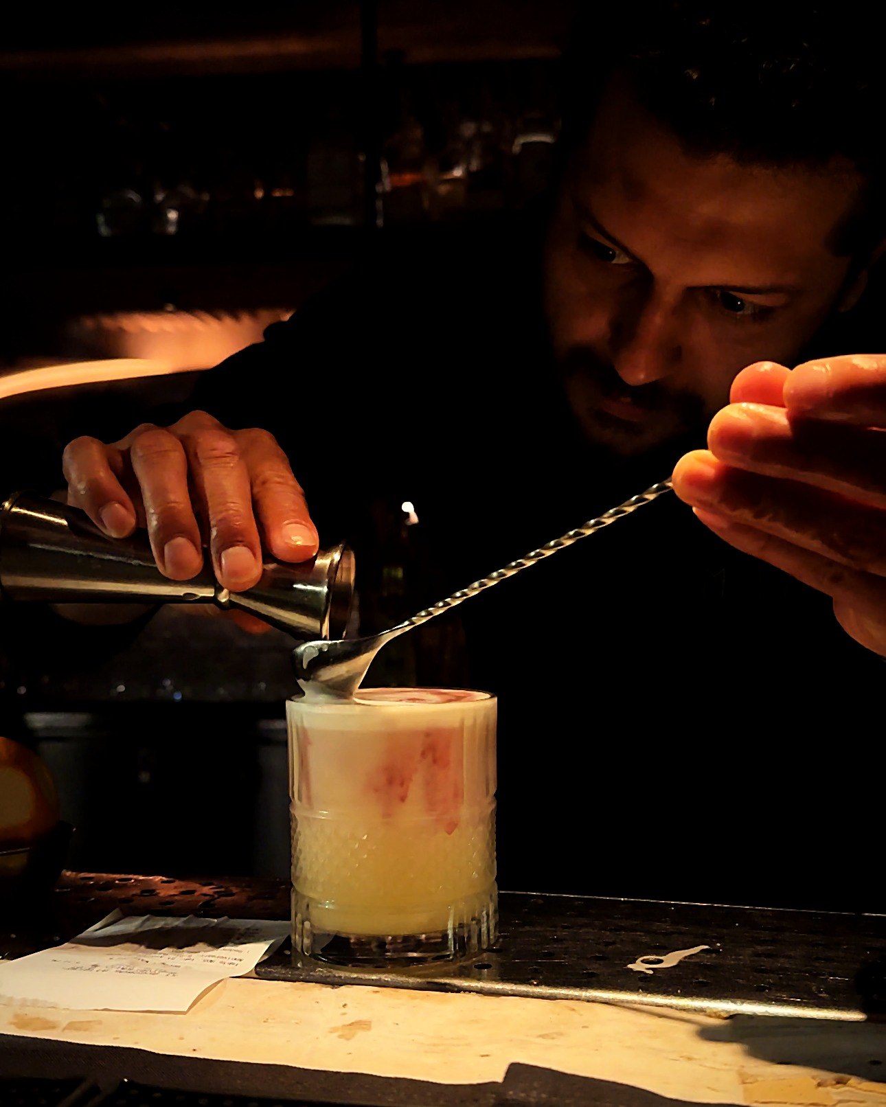 Andres Caro layering a float over a bar spoon behind the bar at Mila