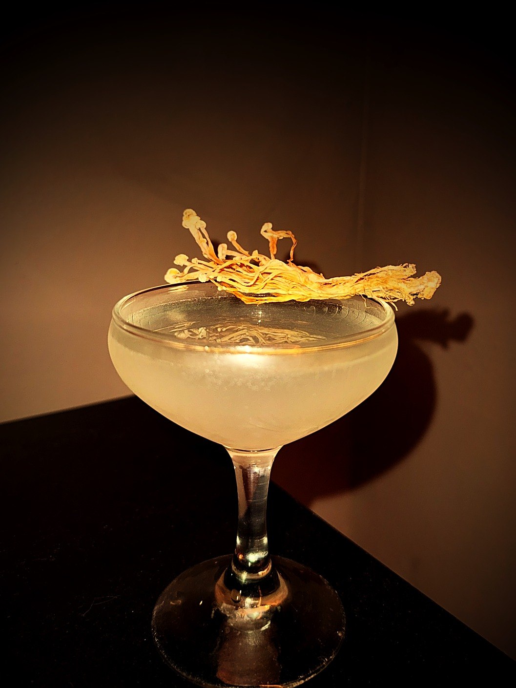 Umami martini in a frosted coupe garnished with dehydrated enoki mushroom